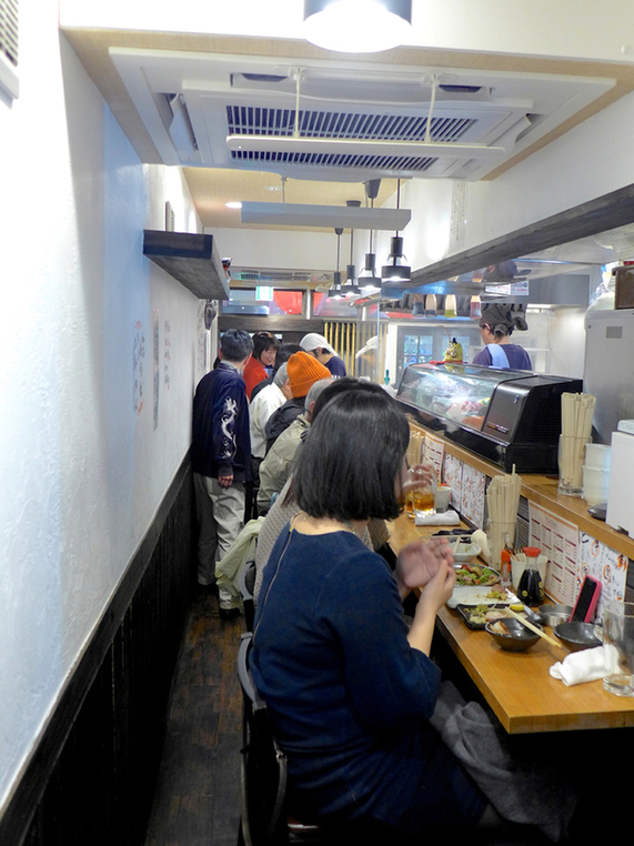 カウンターで一人飲みを楽しむ客とスタッフとの交流シーン